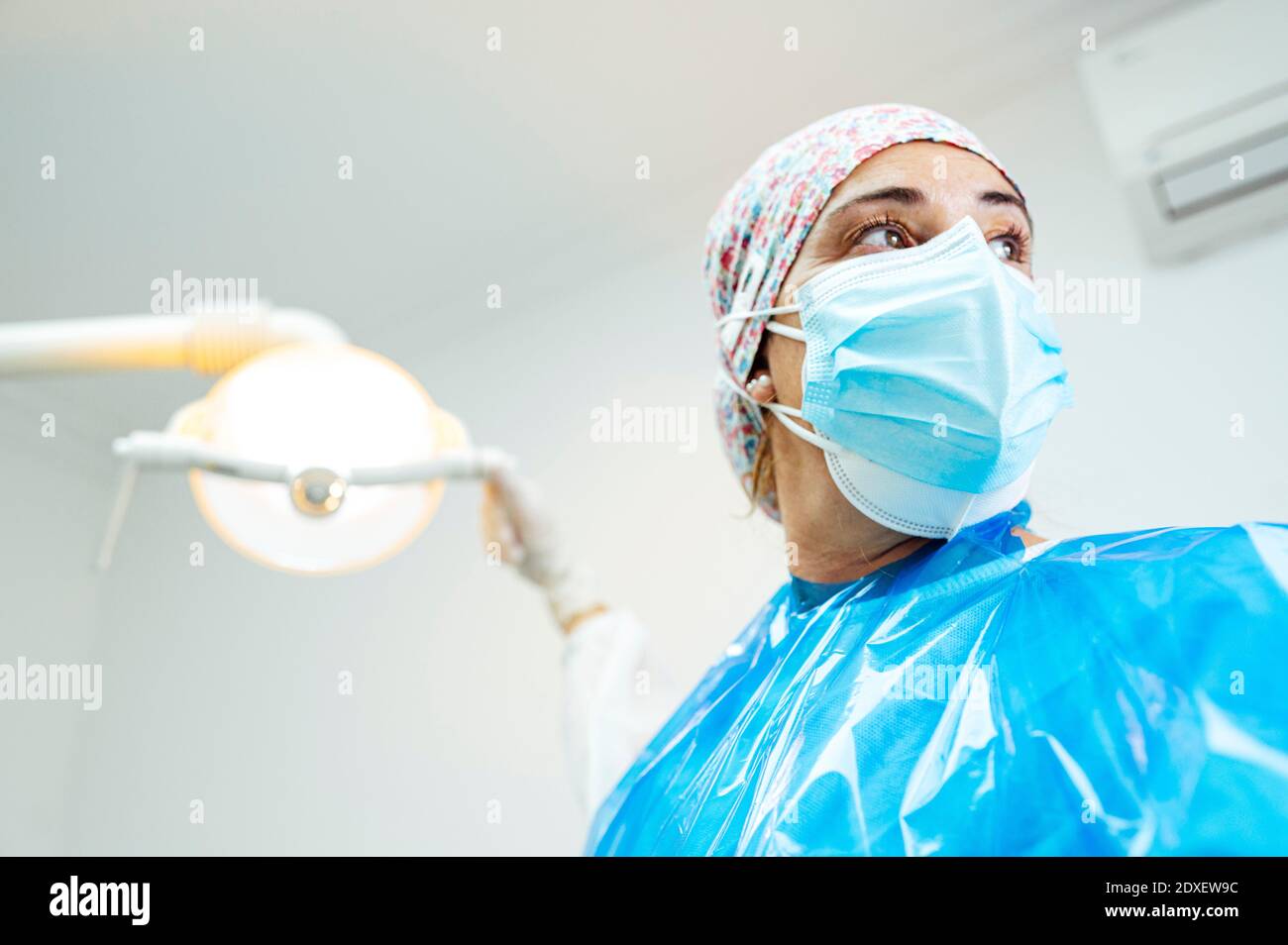 Zahnarzt trägt schützende Arbeitskleidung, die wegschaut, während sie steht Medizinische Klinik Stockfoto