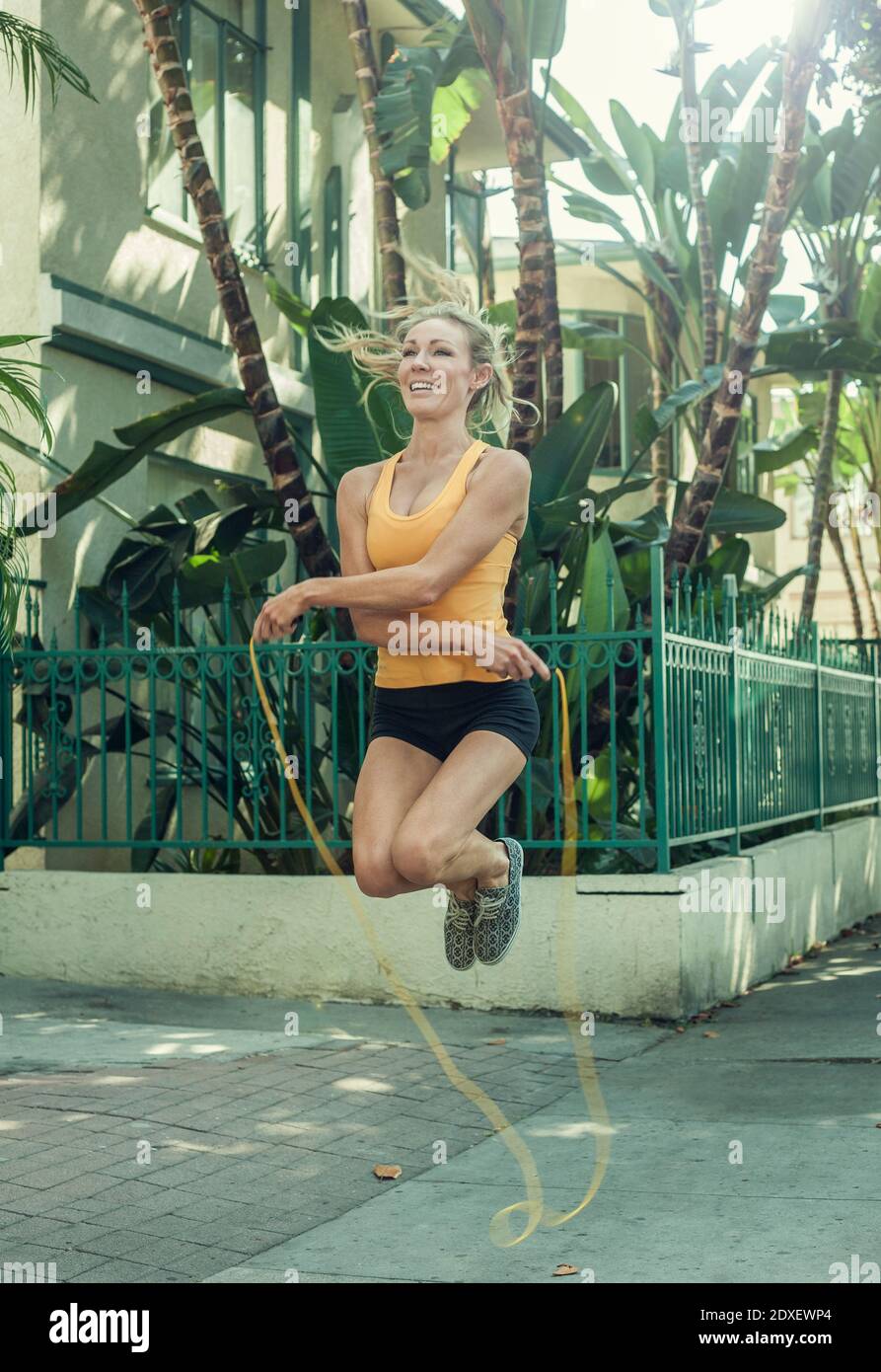 Glückliche junge Frau springt mit Springseil über Bürgersteig hinein Morgen Stockfoto