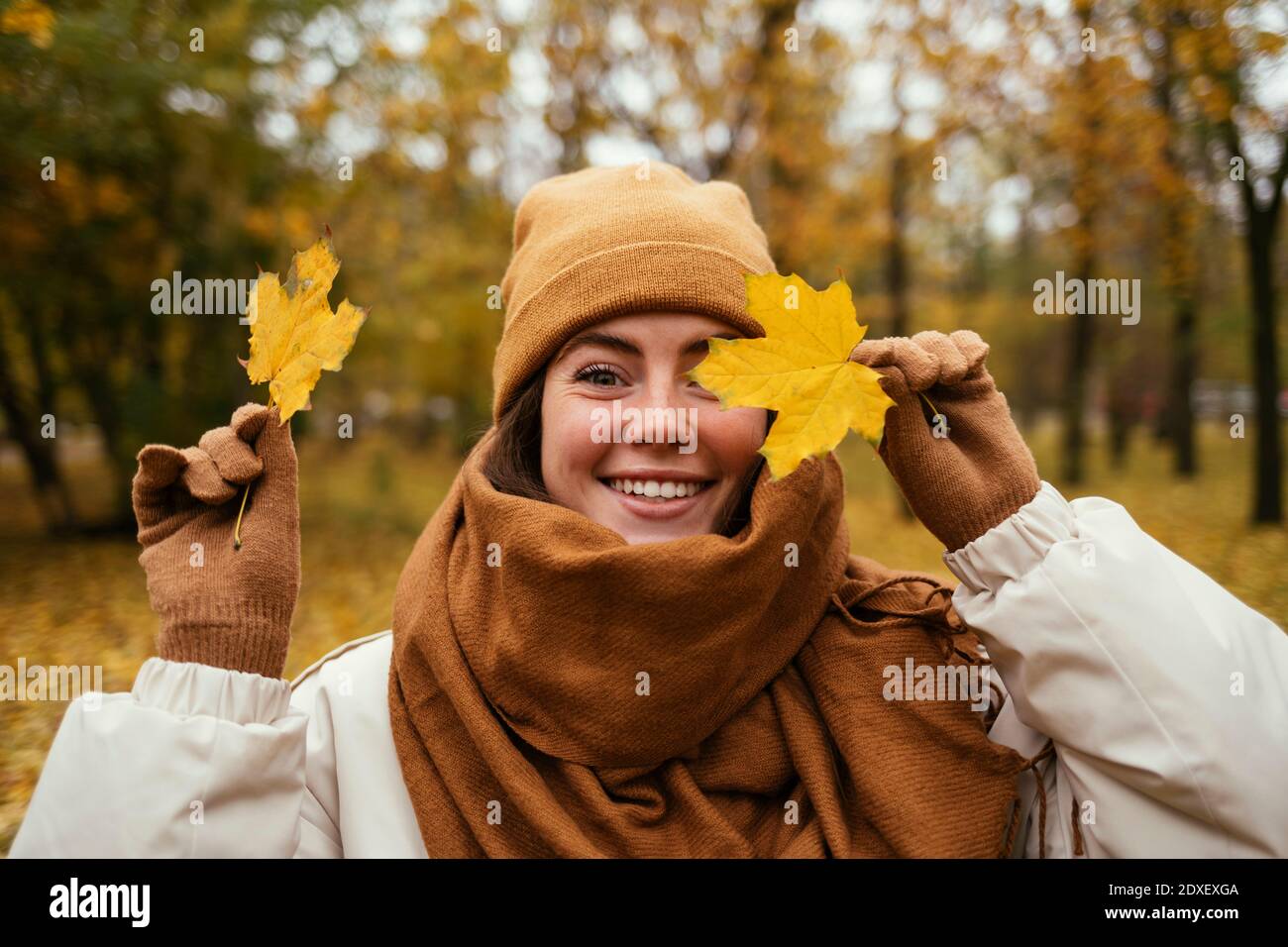 Glückliche junge Frau, die das Auge mit Herbstblatt in der Öffentlichkeit bedeckt parken Stockfoto