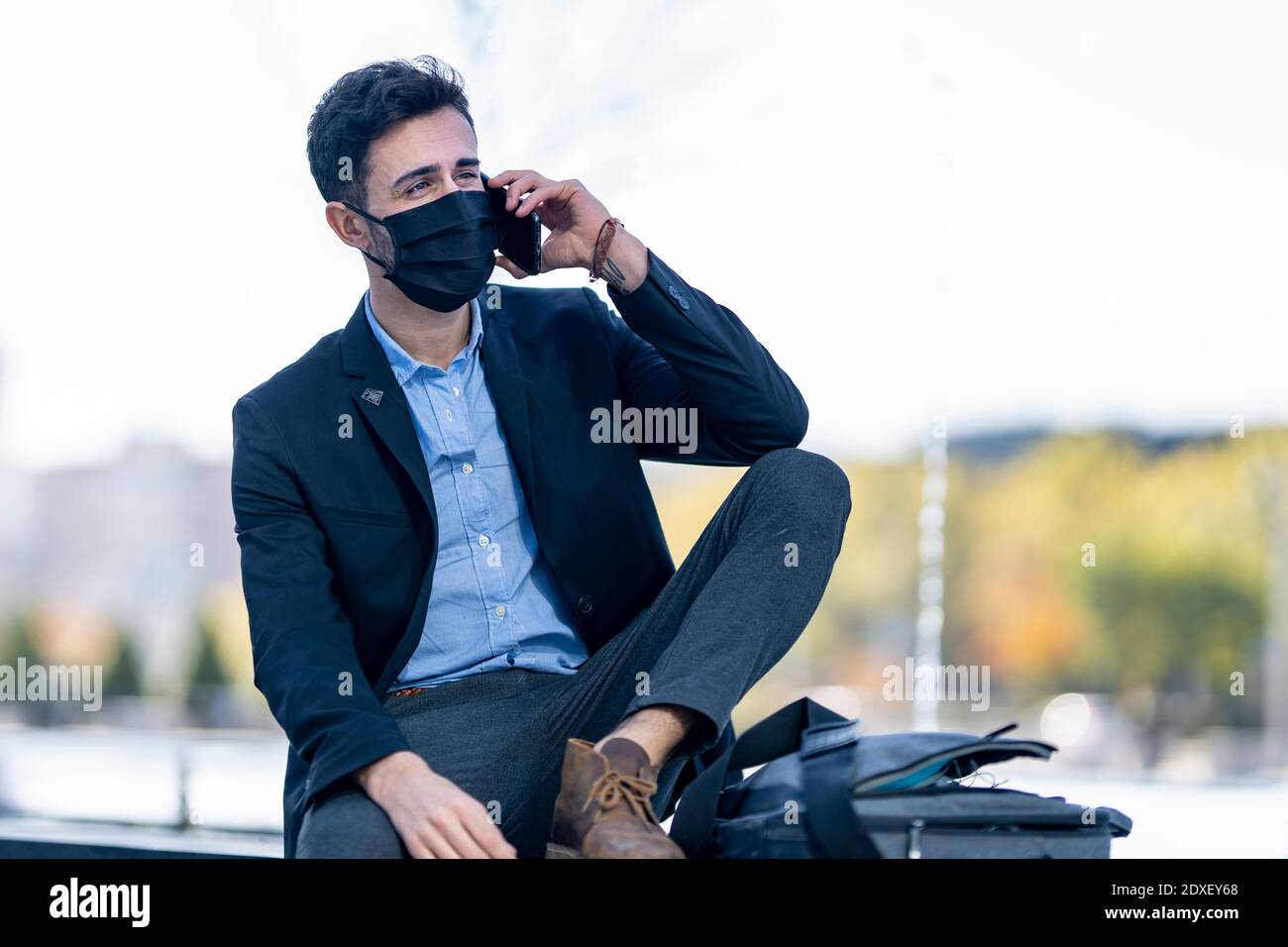 Geschäftsmann trägt Schutzmaske im Gespräch auf Handy, während Draußen sitzen Stockfoto