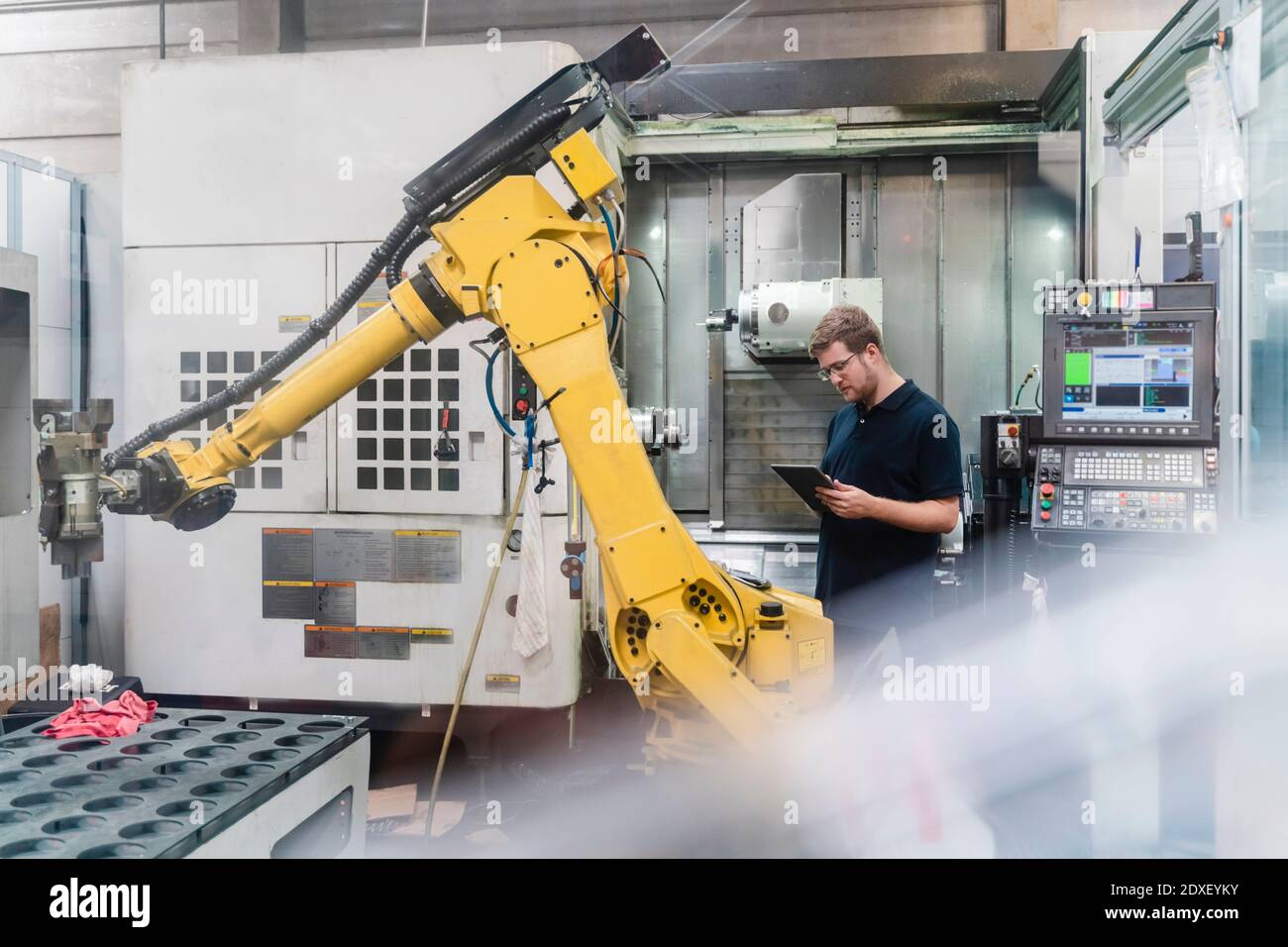 Arbeiter in der Fabrik, der ein digitales Tablet benutzt, während er vor dem Hotel steht Von Roboterarmen in der Industrie Stockfoto
