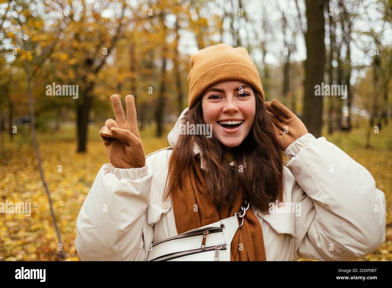Schöne Frau, die Friedenszeichen tut, während sie im Herbstpark steht Stockfoto