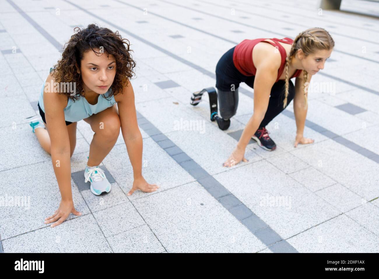 Sportlerin, die beim Amputierten hockt, um auf dem Fußweg ein Sportrennen zu machen Stockfoto