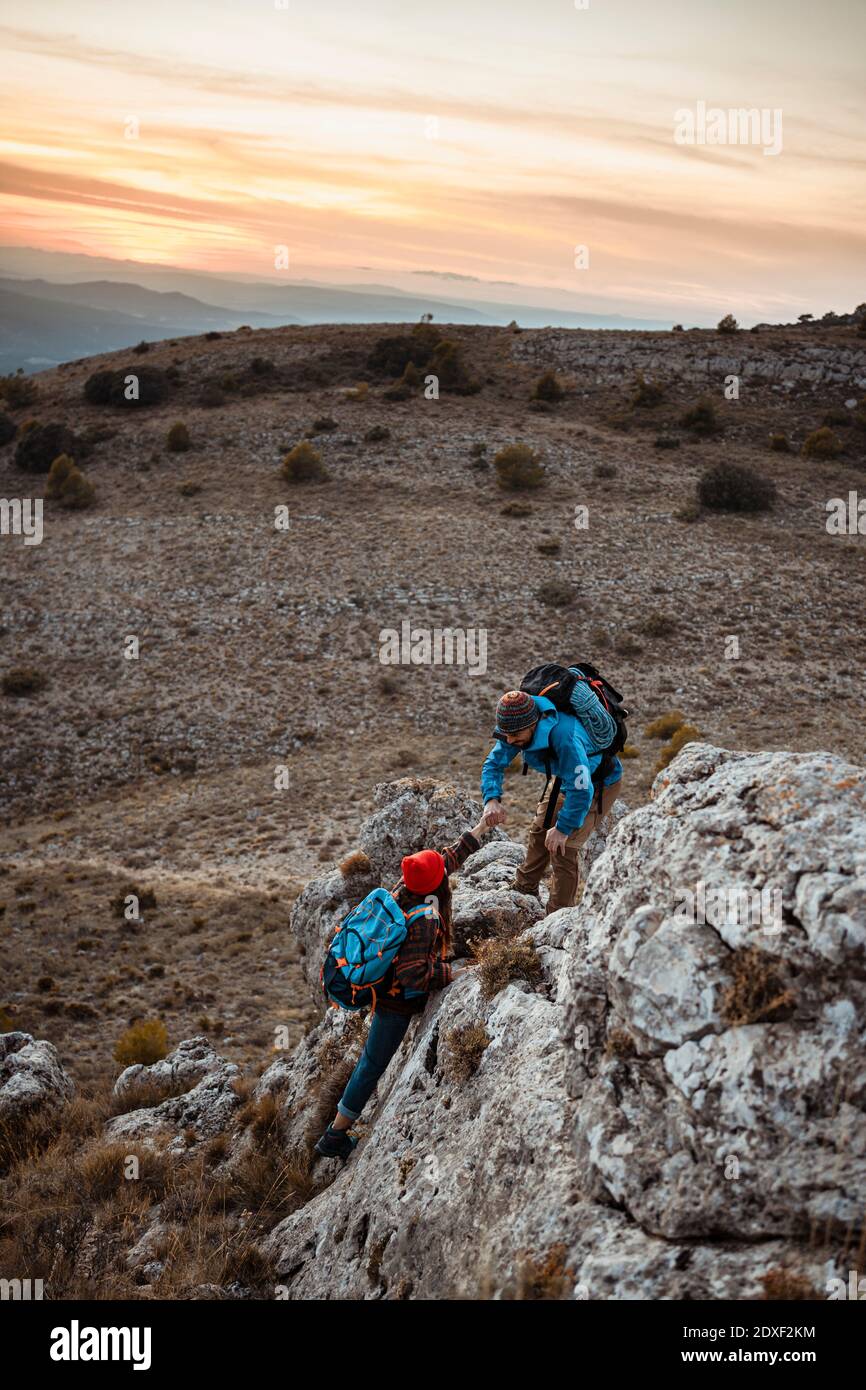 Freund hilft Freundin zu klettern Felsen auf Berg während Sonnenuntergang Stockfoto