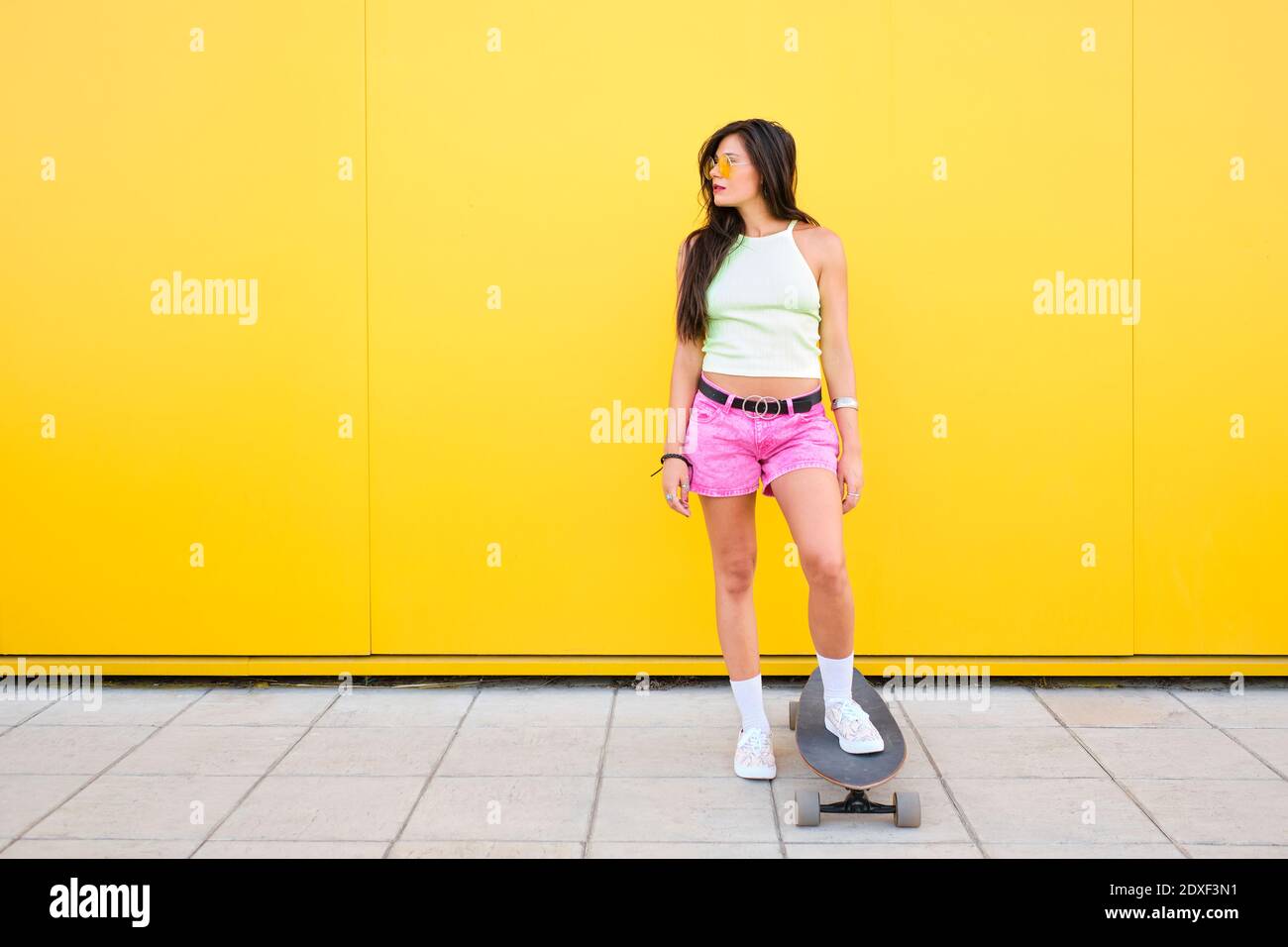 Portrait von schönen Mädchen stehen mit Skateboarding vor Gelbe Wand Stockfoto