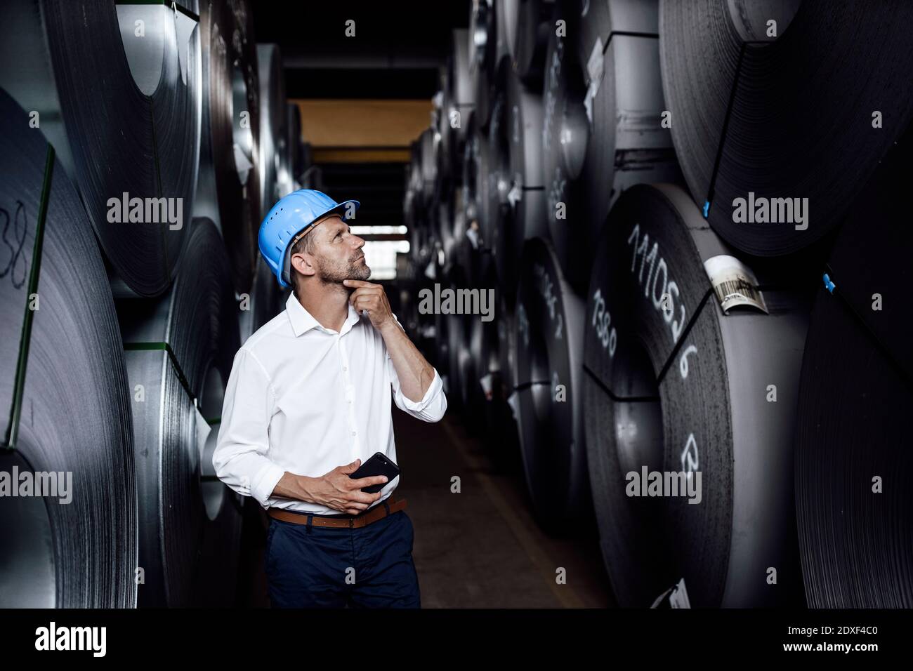 Nachdenklicher Geschäftsmann mit der Hand am Kinn, der in der Fabrik steht Stockfoto