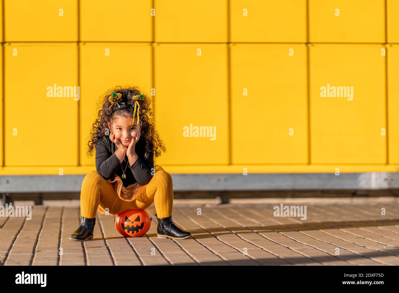 Mädchen sitzt mit Kopf in den Händen auf Halloween Blumentopf Gegen gelb karierte Musterwand Stockfoto