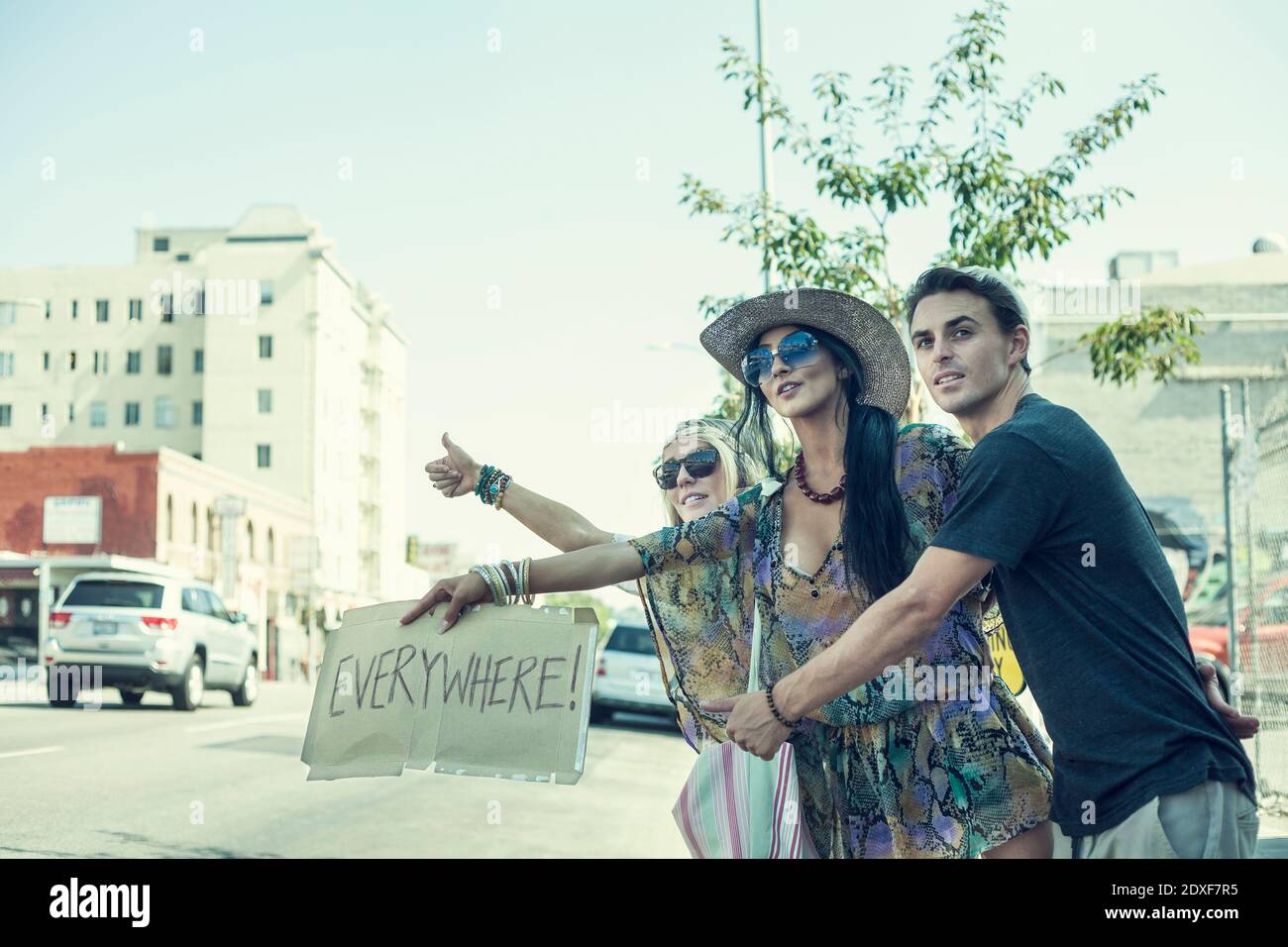 Unbeschwerte Freunde, die beim Anhalten von Plakat mit Text gegen den Himmel trampeln In der Stadt Stockfoto