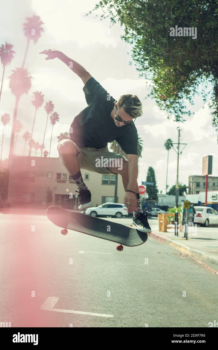 Sorgloser junger Mann dreht Skateboard in der Luft auf der Straße Stockfoto