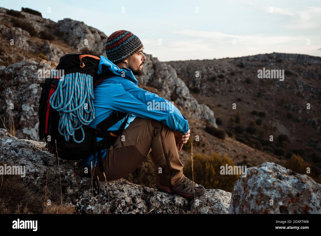 Mittelerwachsener Mann mit Blick auf die Aussicht, während er auf Felsen sitzt Im Urlaub am Berg Stockfoto