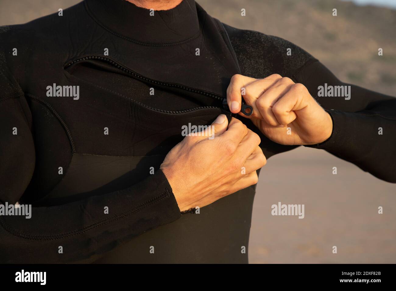 Mann Zipping schwarzen Neoprenanzug am Strand Stockfoto