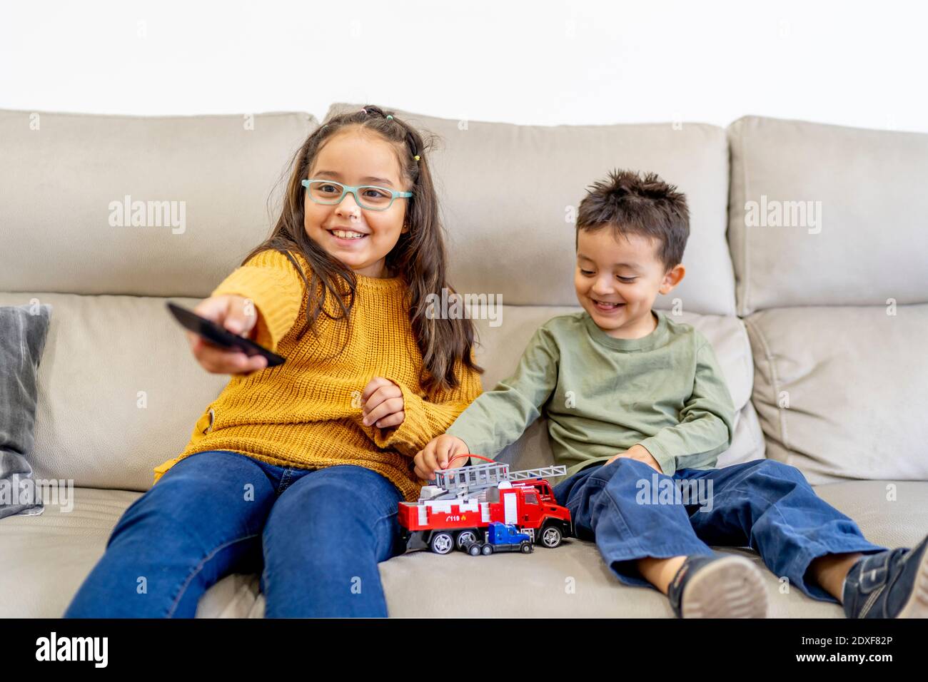 Schwester beim Fernsehen, während Bruder mit Feuerwehrspielzeug spielt Auf dem Sofa zu Hause Stockfoto
