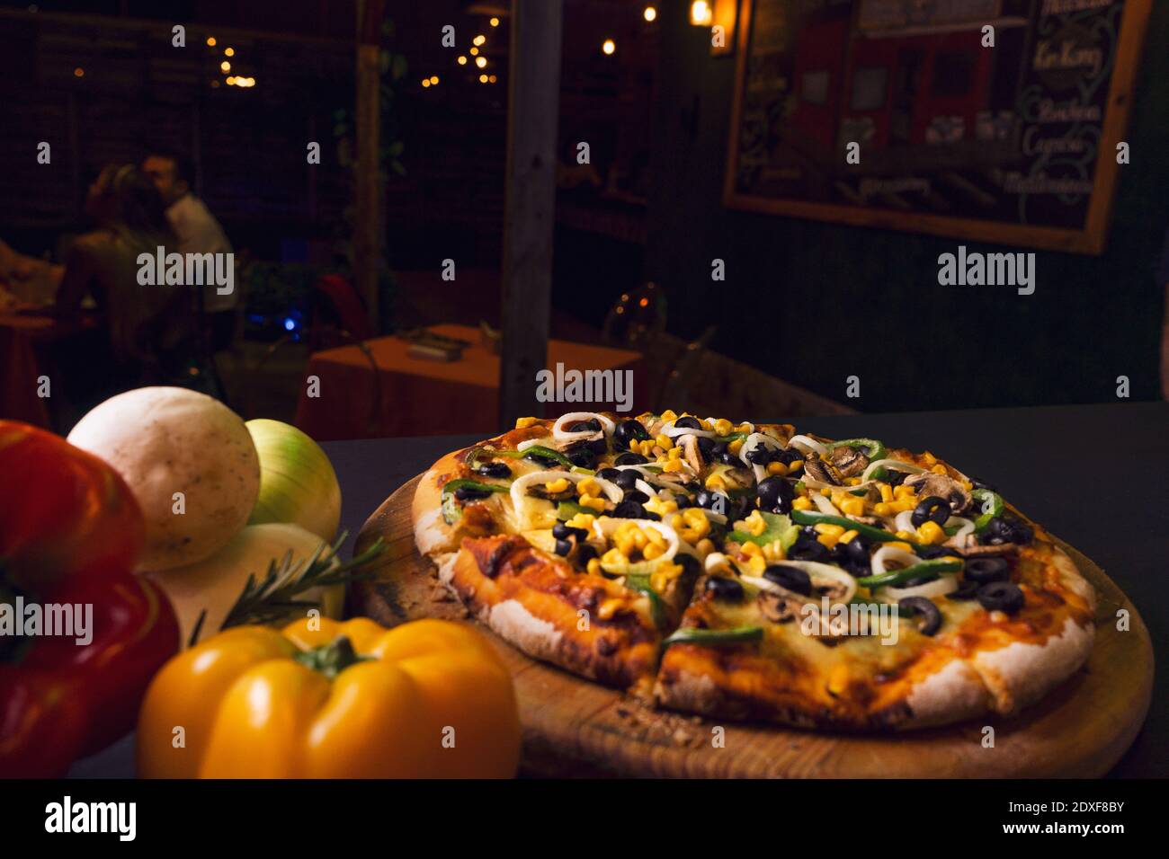 Draufsicht authentische italienische Pizza mit schwarzen Oliven und Gemüse rustikalen schwarzen Holzhintergrund. Blick von oben auf heiße Pizza. Restaurant verwischen Hintergrund Stockfoto