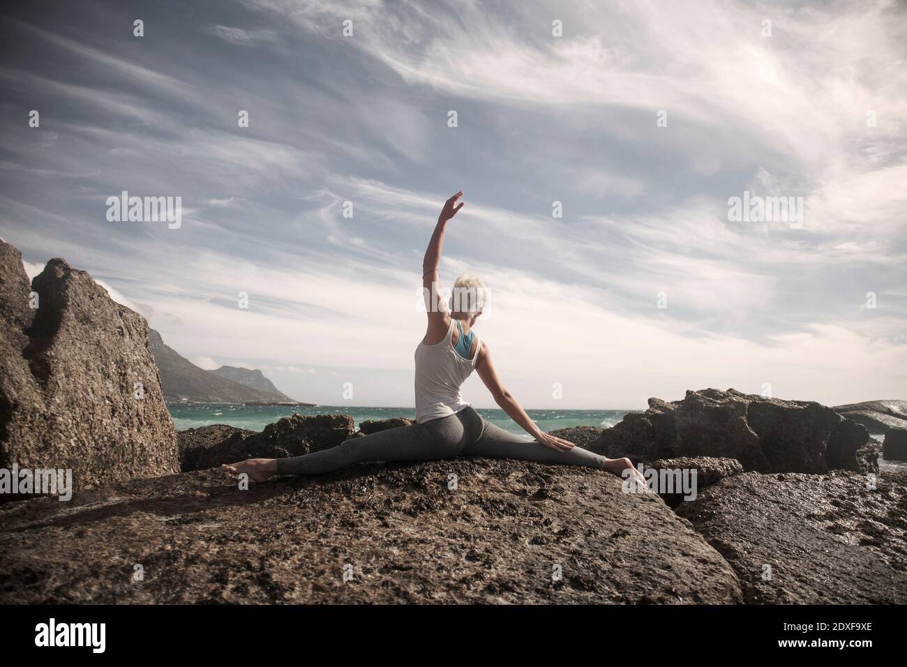 Frau mit gespreizten Beinen und erhobener Hand beim Yoga Felsformation Stockfoto