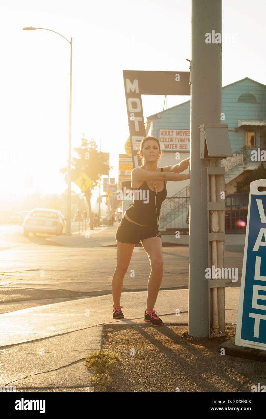 Junge Frau Stretching durch Stange auf Bürgersteig in der Stadt während Sonnenuntergang Stockfoto