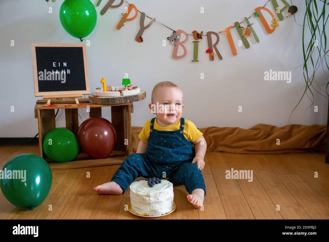 Lächelnder Junge, der mit Kuchen auf dem Boden gegen die Dekoration sitzt Zu Hause Stockfoto