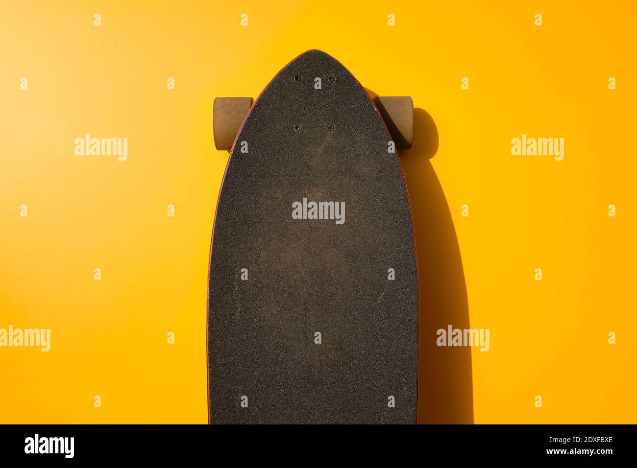 Schwarzes Longboard an gelber Wand Stockfoto