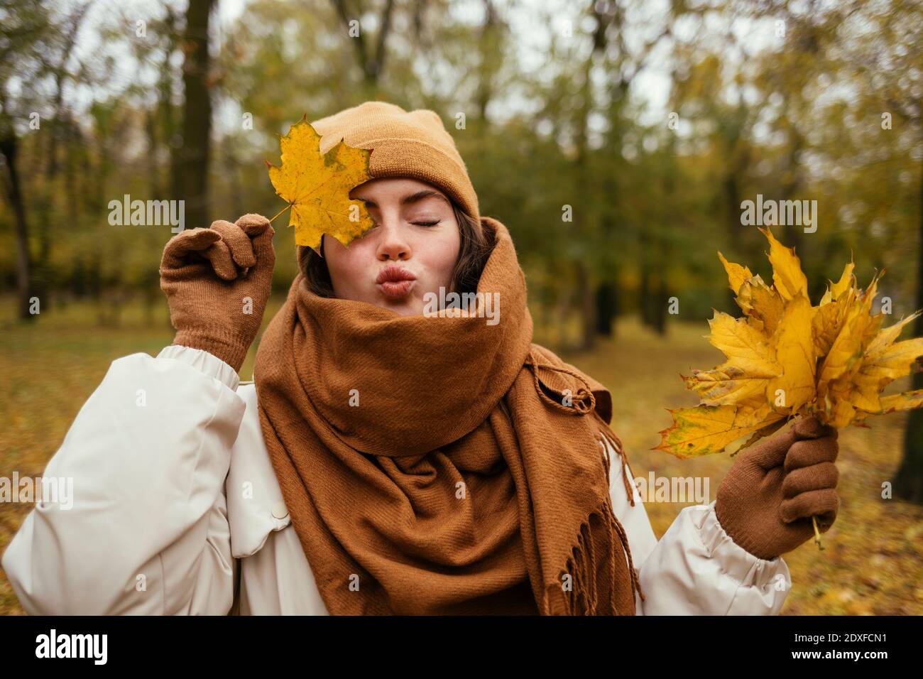 Junge Frau mit geschlossenen Augen Puckering während der Abdeckung Auge mit Herbstblatt im öffentlichen Park Stockfoto