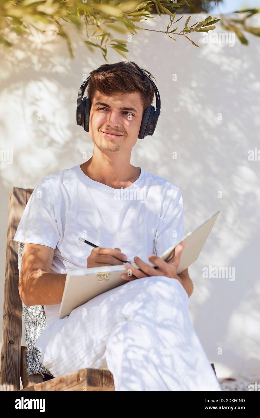 Lächelnder Mann denkt beim Hören von Musik gegen weiße Wand Im Hinterhof Stockfoto