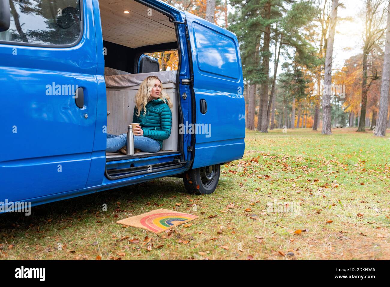 Nachdenkliche Frau hält Tee Tasse, während an der Tür von sitzen Wohnmobil in Cannock Chase Stockfoto