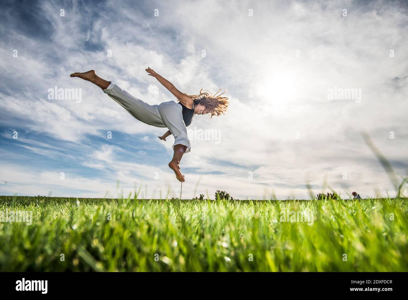 Weibliche Sportlerin springen in der Luft über Gras im Park gegen wolkiger Himmel Stockfoto