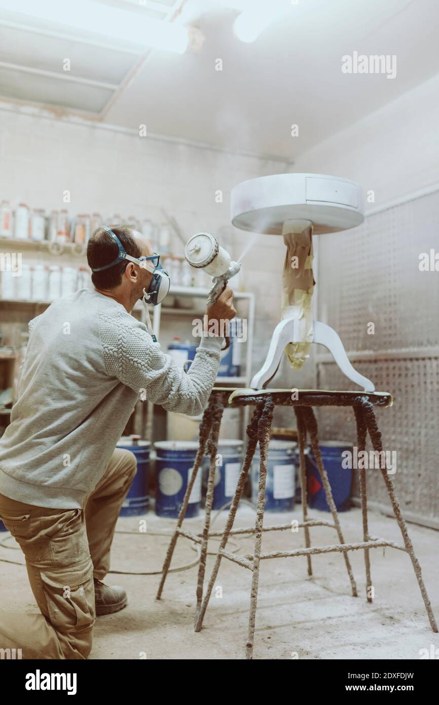 Männliche manuelle Arbeiter Malerei Tisch mit Spritzpistole in der Werkstatt Stockfoto