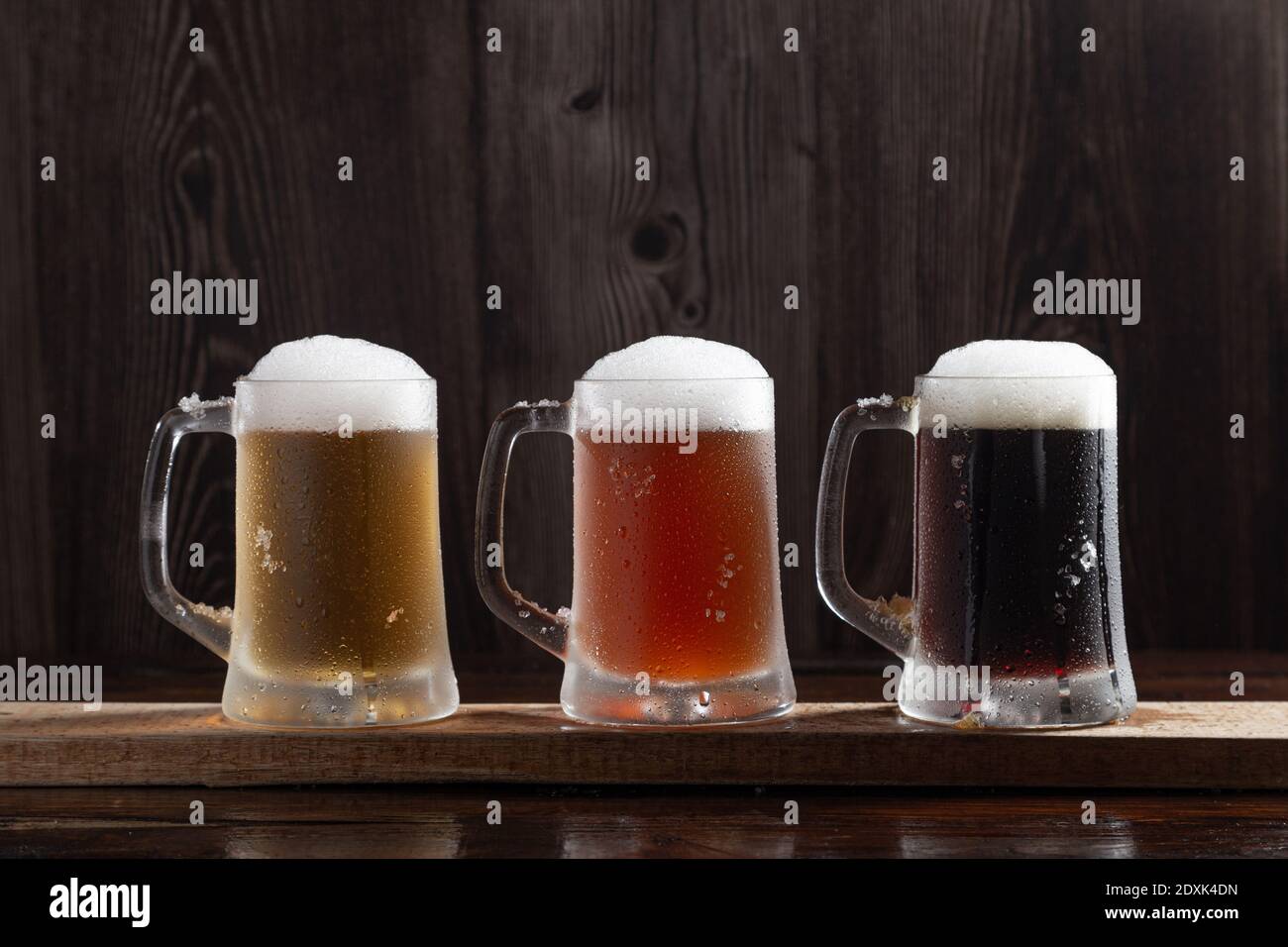 Drei Arten von kaltem Bier in Krügen auf Holzsockel. Stockfoto