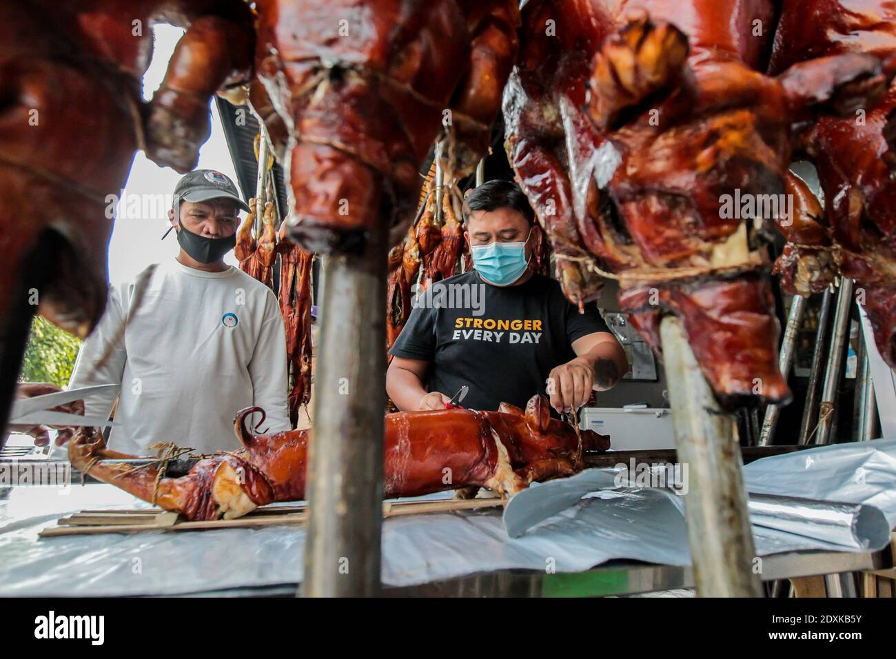 Manila, Philippinen. Dezember 2020. Ein Arbeiter, der eine Gesichtsmaske trägt, schneidet ein gebratenes Schwein in Manila, Philippinen, 24. Dezember 2020. Gebratenes Schwein ist ein Grundnahrungsmittel der philippinischen Familien, besonders beliebt während der Weihnachtsferien. Quelle: Rouelle Umali/Xinhua/Alamy Live News Stockfoto