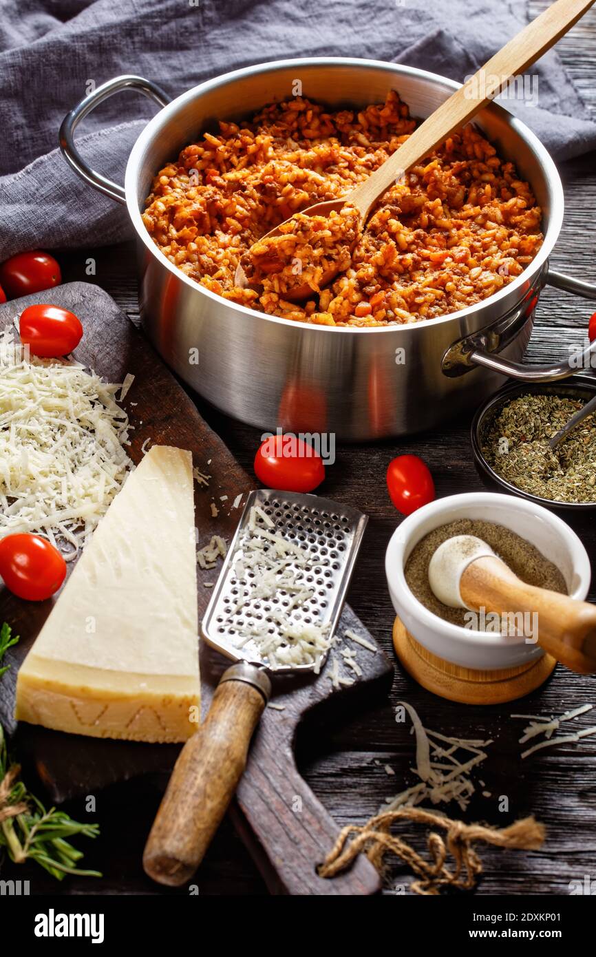 Hackfleisch Risotto in einem Metall Stevpot mit einem Löffel auf einem dunklen Holztisch mit Zutaten, italienische Küche, vertikale Ansicht von oben Stockfoto