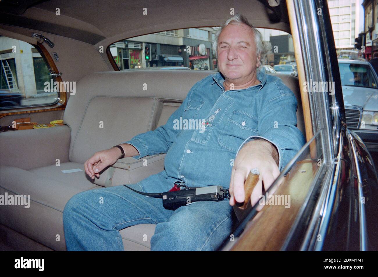 Vintage 1992 Foto zeigt Engländer, Briten, Regisseur Michael Winner, der sich in seinem Rolls Royce Motor Car zurücklehnen, eine Zigarre rauchen und Denim tragen kann. Foto aufgenommen in London. Stockfoto