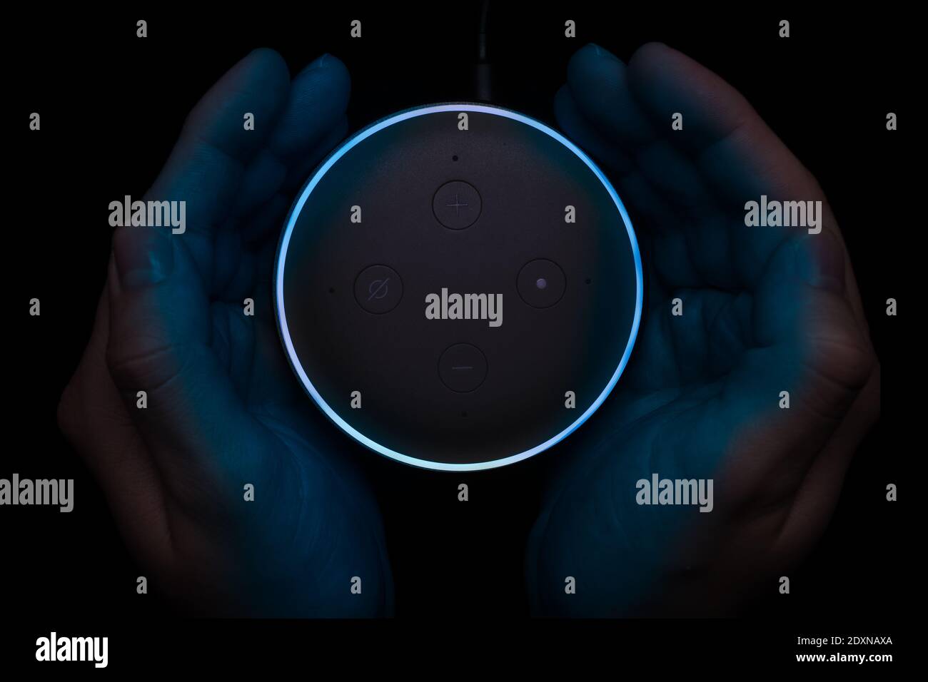 London, Vereinigtes Königreich - Dezember 19 2020: Hände um einen beleuchteten Amazon Echo Dot Smart Speaker mit eingebautem Alexa Voice Assistant. Stockfoto