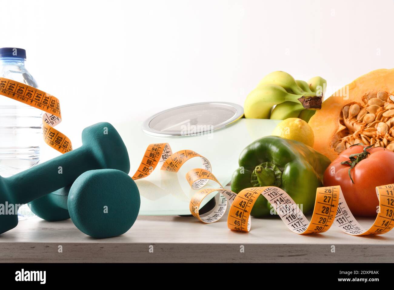 Gesundes Lifestyle-Konzept mit Gemüse und Obst auf dem Tisch mit Hanteln und Waage und Messgerät zur Körperkontrolle mit isoliertem weißem Hintergrund. Stockfoto