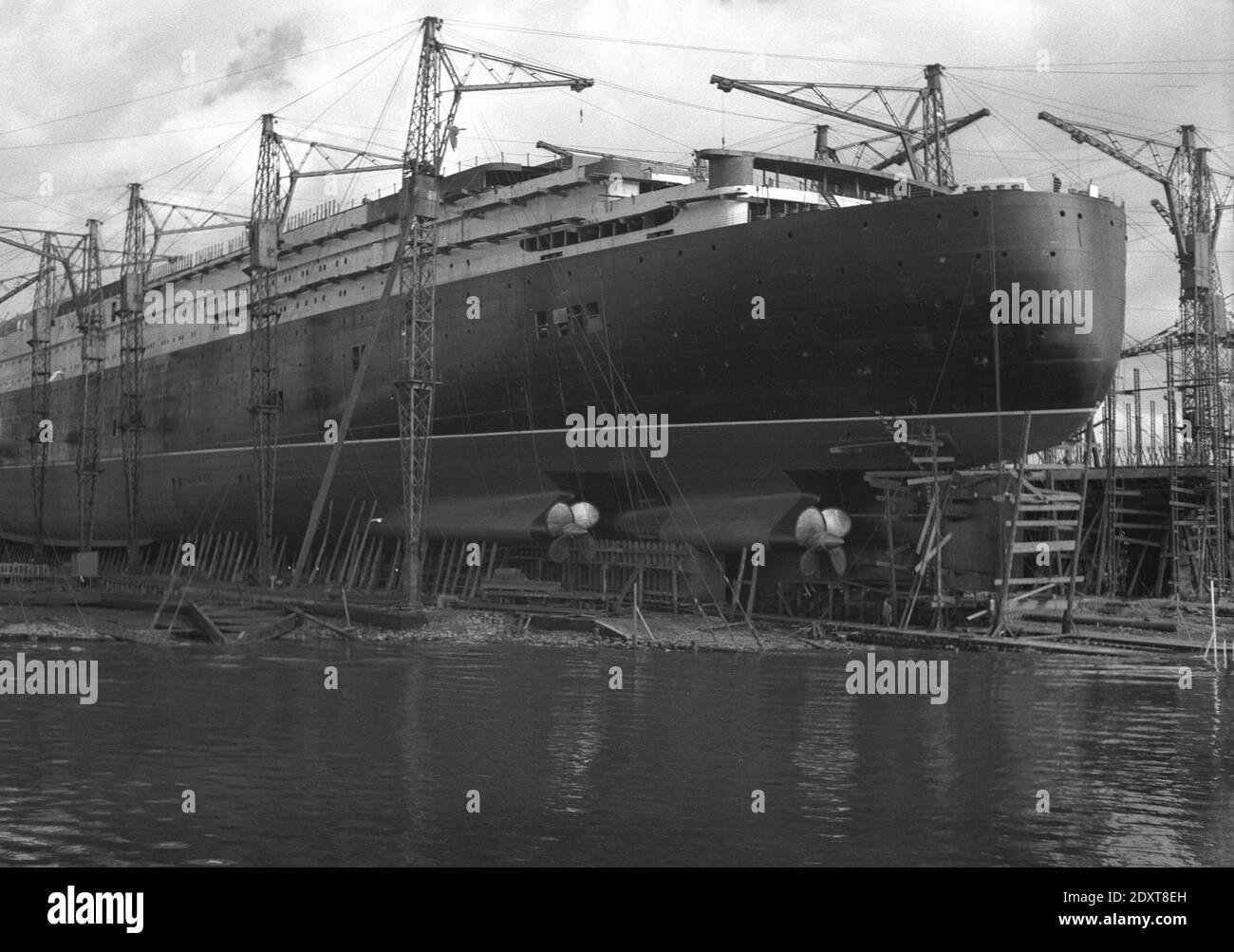 1930er Jahre, historisch, die RMS Queen Elizabeth im Bau auf dem Clyde, Glasgow, Schottland. UK. Benannt nach der Ehefrau von König Georg VI. War sie das größte Passagierschiff, das zu dieser Zeit gebaut wurde. Obwohl sie 1938 offiziell gestartet wurde, bedeutete der Ausbruch des 2. Weltkriegs, dass sie während der Feindseligkeiten zu einem Truppenschiff umgebaut wurde, bevor sie 1948 ihre erste Reise unternahm. Sie wurde 1968 in den Ruhestand versetzt. Stockfoto