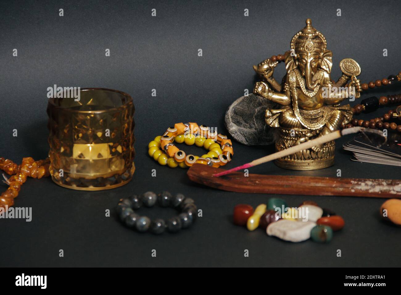 Okkulter Altar mit Gottesfigur Ganesha, Kerzen, Duftstäbchen, Steinen, trockenen Kräutern. Schwarzer Hintergrund. Stockfoto