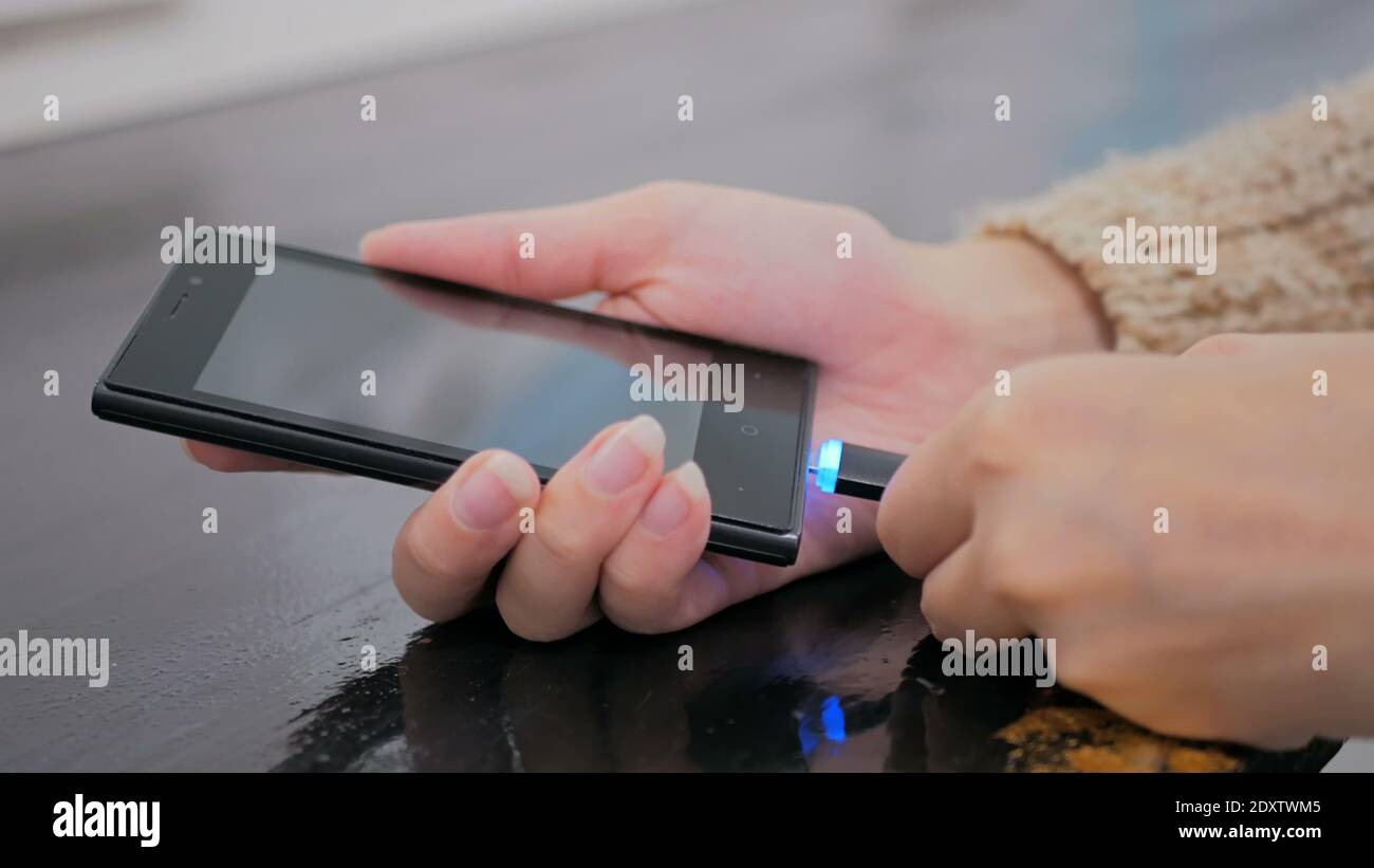 Woman's Hand stecken schwarze Blitz Ladekabel in Smartphone Stockfoto