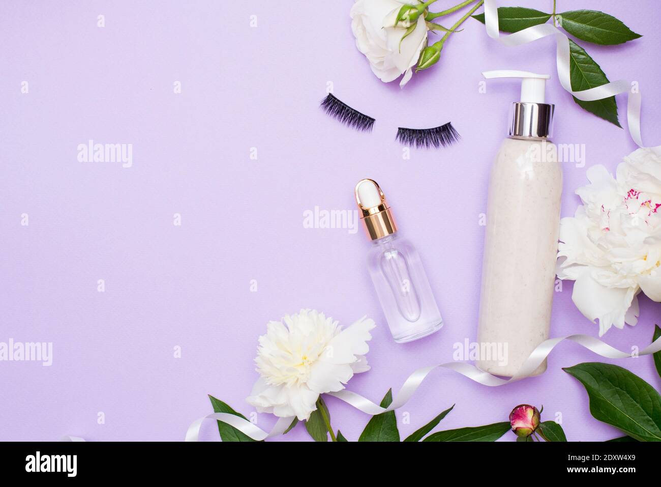 Beauty Flat Lay mit kosnetischem Öl, Lotion und falschen Wimpern mit Blumen, Hintergrund mit Freitext Space Stockfoto