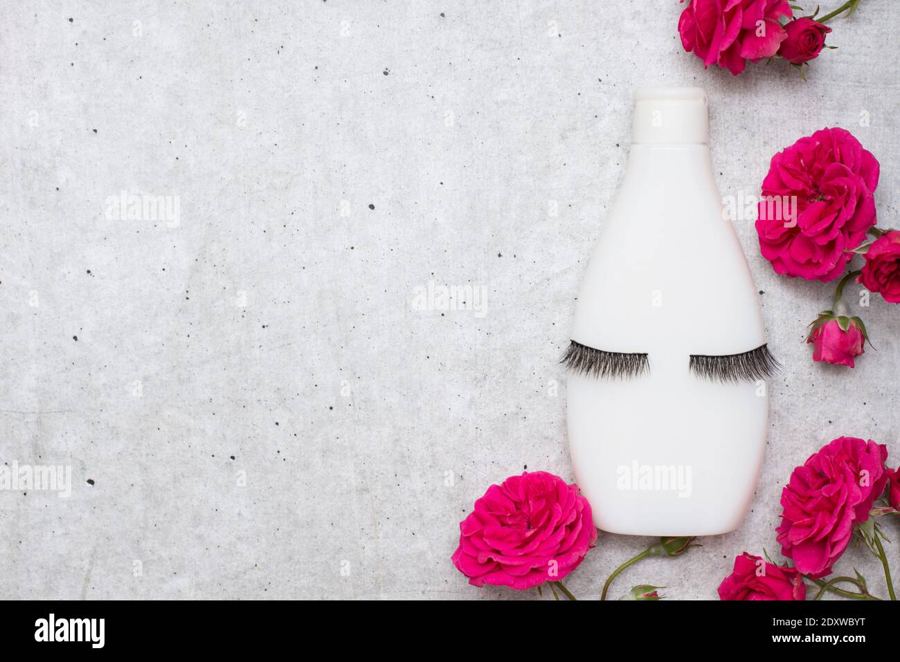 Weiße Flasche für Shampoo und Kosmetik mit falschen Wimpern und Rote Blumen auf grauem Hintergrund mit Kopierraum Stockfoto