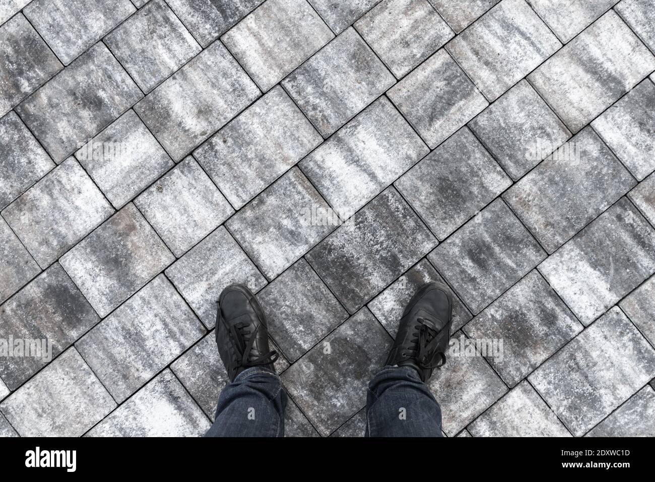 Männliche Füße in Jeans und schwarze Schuhe stehen auf grauem Steinpflaster, Draufsicht Stockfoto