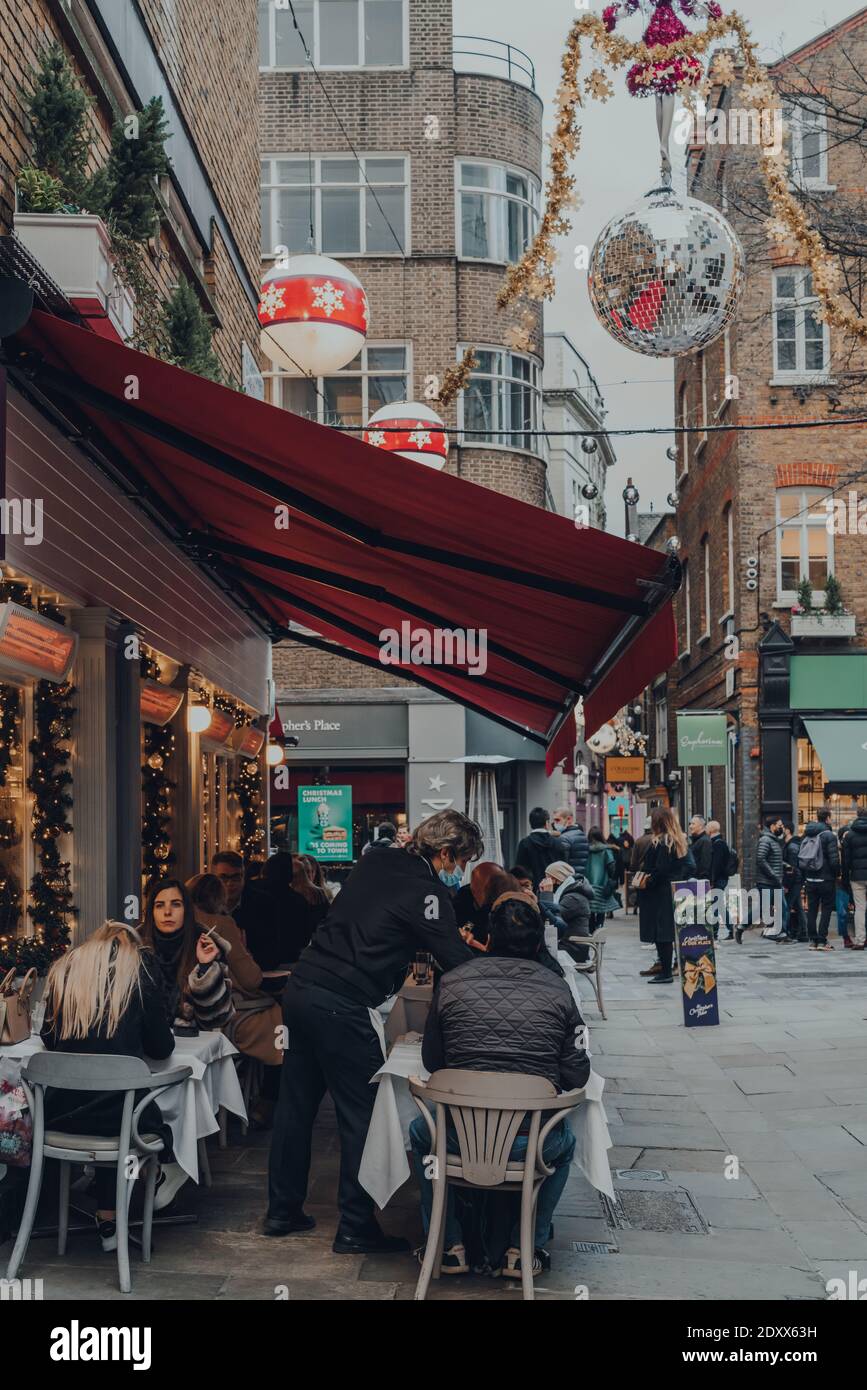 London, Großbritannien - Dezember 5,2020: Kellner in Gesichtsmaske, die Menschen an den Tischen im Freien eines Restaurants in St Christopher's Place, einem lebhaften Stadtquar, bedienen Stockfoto