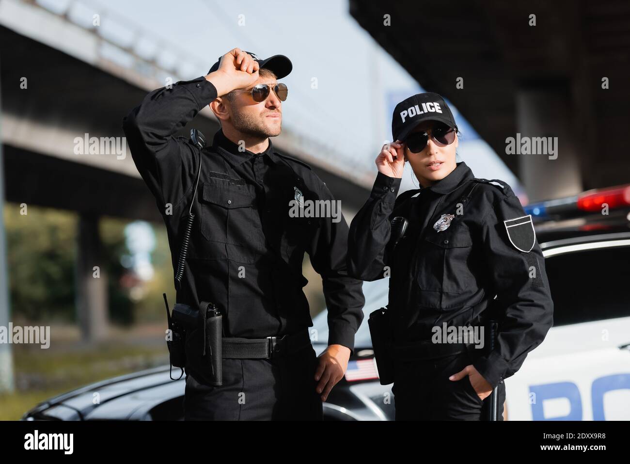 Polizeibeamte in Sonnenbrillen stehen in der Nähe des Autos auf unscharfem Hintergrund Im Freien Stockfoto