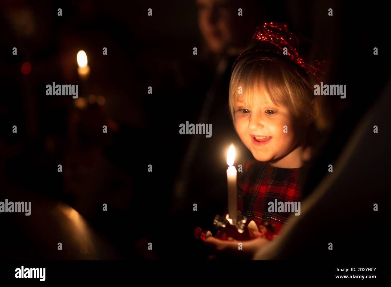 Cradley Heath, West Midlands, Großbritannien. Dezember 2020. Die dreijährige Harlow Hadlington blickt aufgeregt auf ihre Christingle Orange während des Weihnachtsgottesdienstes für Kinder in der Holy Trinity Church, Cradley Heath, West Midlands. Im Christingle-Gottesdienst repräsentiert die Orange die Welt, das rote Band symbolisiert die Liebe und das Blut Christi, die Süßigkeiten stellen alle Schöpfungen Gottes dar, und die brennende Kerze stellt das Licht Jesu in der Welt dar und bringt den Menschen, die in der Dunkelheit leben, Hoffnung. Kredit: Peter Lopeman/Alamy Live Nachrichten Stockfoto