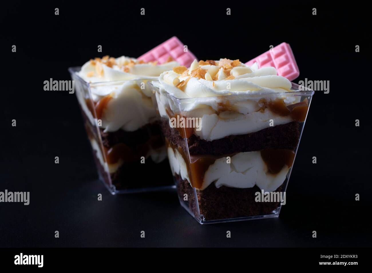 Kleinigkeiten aus Schokoladenkeks mit Karamell-Erdnussfüllung auf schwarzem Hintergrund. Dessert ist mit cremiger Käsecreme und rosa Schokolade dekoriert Stockfoto