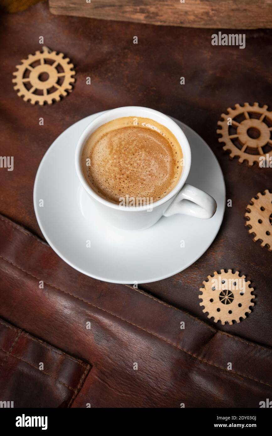 Porzellanbecher mit einem leckeren Espresso ist auf dem Tisch mit einem Ledertuch mit separaten hölzernen Dekor Details der Mechanismen bedeckt. Restaurant Stockfoto