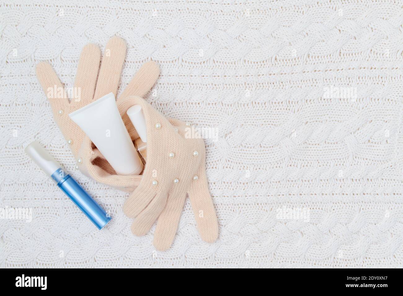 Winter flach legen mit Handcreme, Nagellack und Handschuhe auf weißem gestrickten Hintergrund. Stockfoto