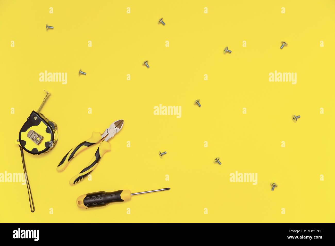 Eine Flachlage mit einem Satz von Tischwerkzeugen, Schraubendreher, Schneidzange, Maßband und Schrauben auf gelb leuchtenden Hintergrund. Farben des Jahres 2021. Stockfoto