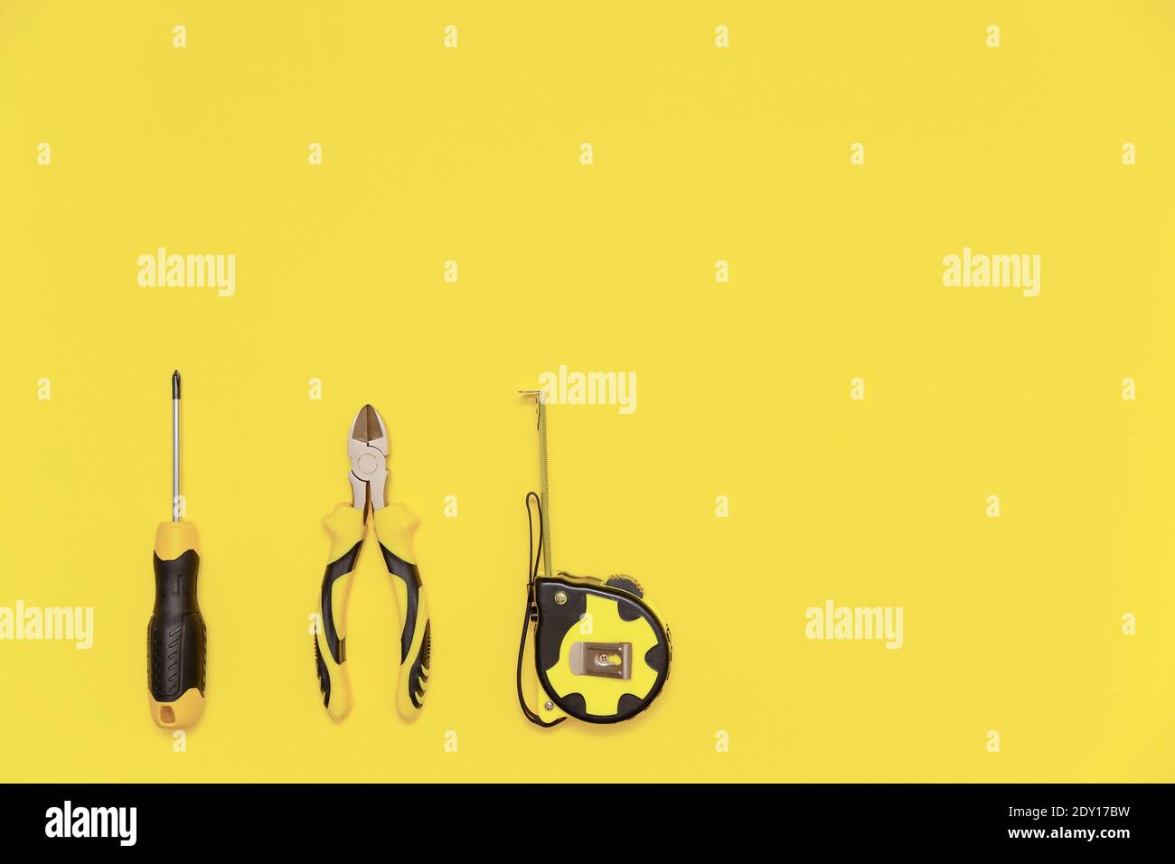 Eine Flachlage mit einem Satz von Tischwerkzeugen, Schraubendreher, Schneidzange und Band messen auf gelb leuchtenden Hintergrund. Farben des Jahres 2021. Stockfoto