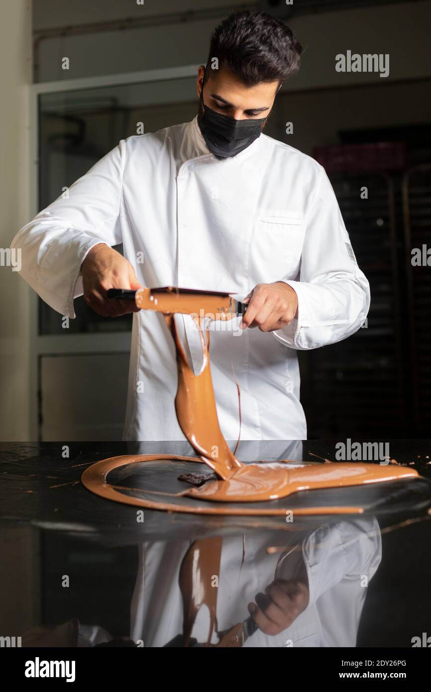 Junger Konditor mit Maske, der auf das Temperieren von Schokolade arbeitet. Stockfoto