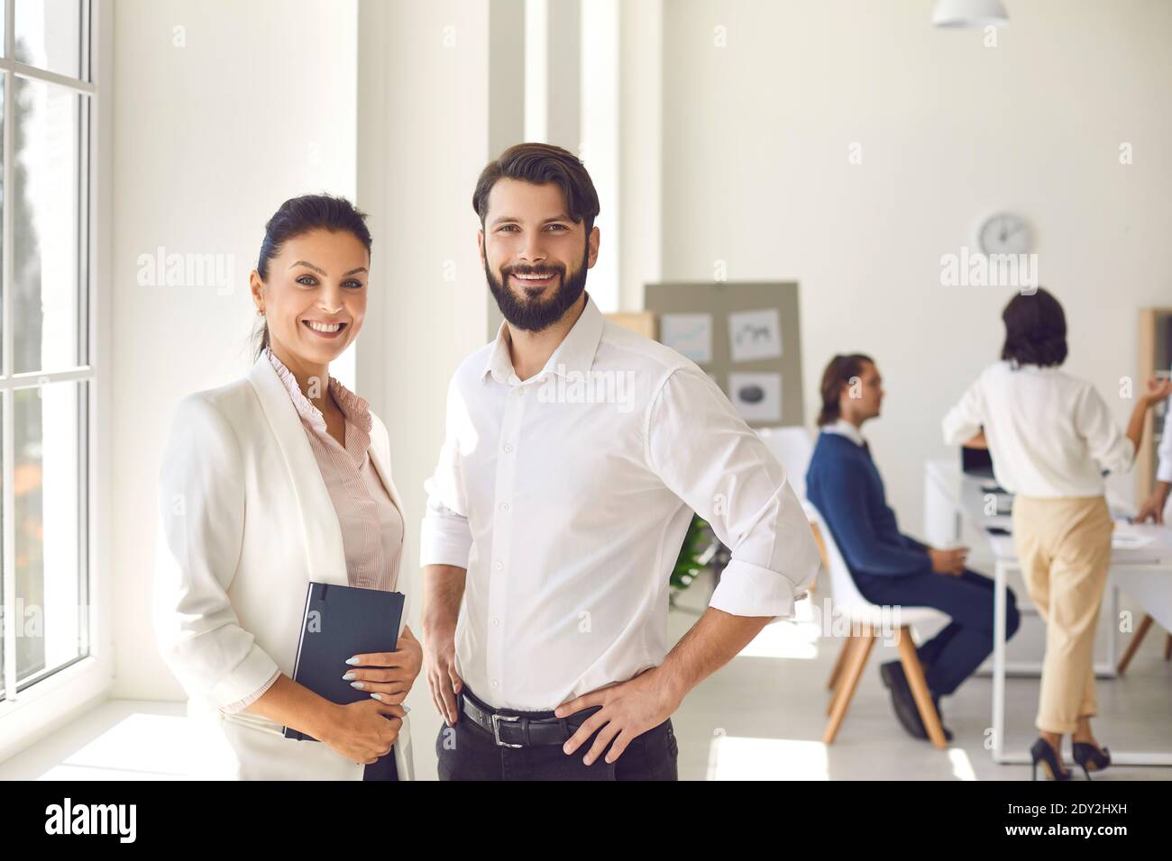 Porträt einer selbstbewussten Frau und eines Mannes, die vor dem Hintergrund der Arbeiter in der Bürohalle stehen. Stockfoto