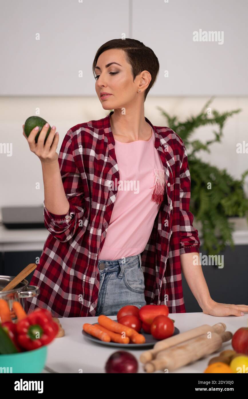 Mit Blick auf Avocado und denken hübsche Hausfrau mit einer kurzen Frisur bereitet Essen in der Küche. Gesunde Ernährung zu Hause. Gesunde Ernährung verlassen - Stockfoto