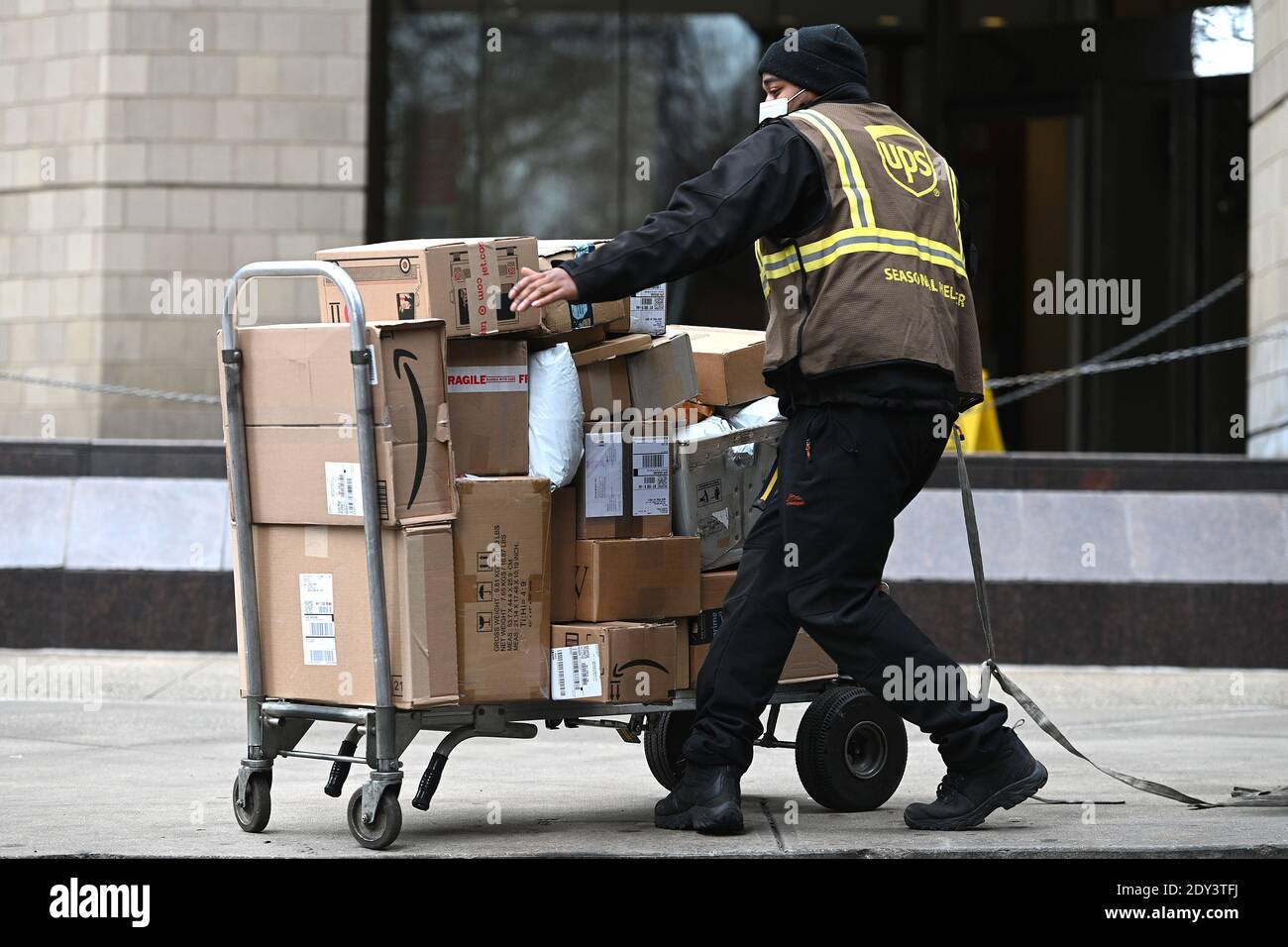New York, USA. Dezember 2020. Ein UPS-Mitarbeiter bewegt einen Handwagen,  der mit Paketen gestapelt ist, die am 24. Dezember 2020 in New York, NY,  geliefert werden sollen. Mit einem Wiederaufleben von COVID-19-Infektionen